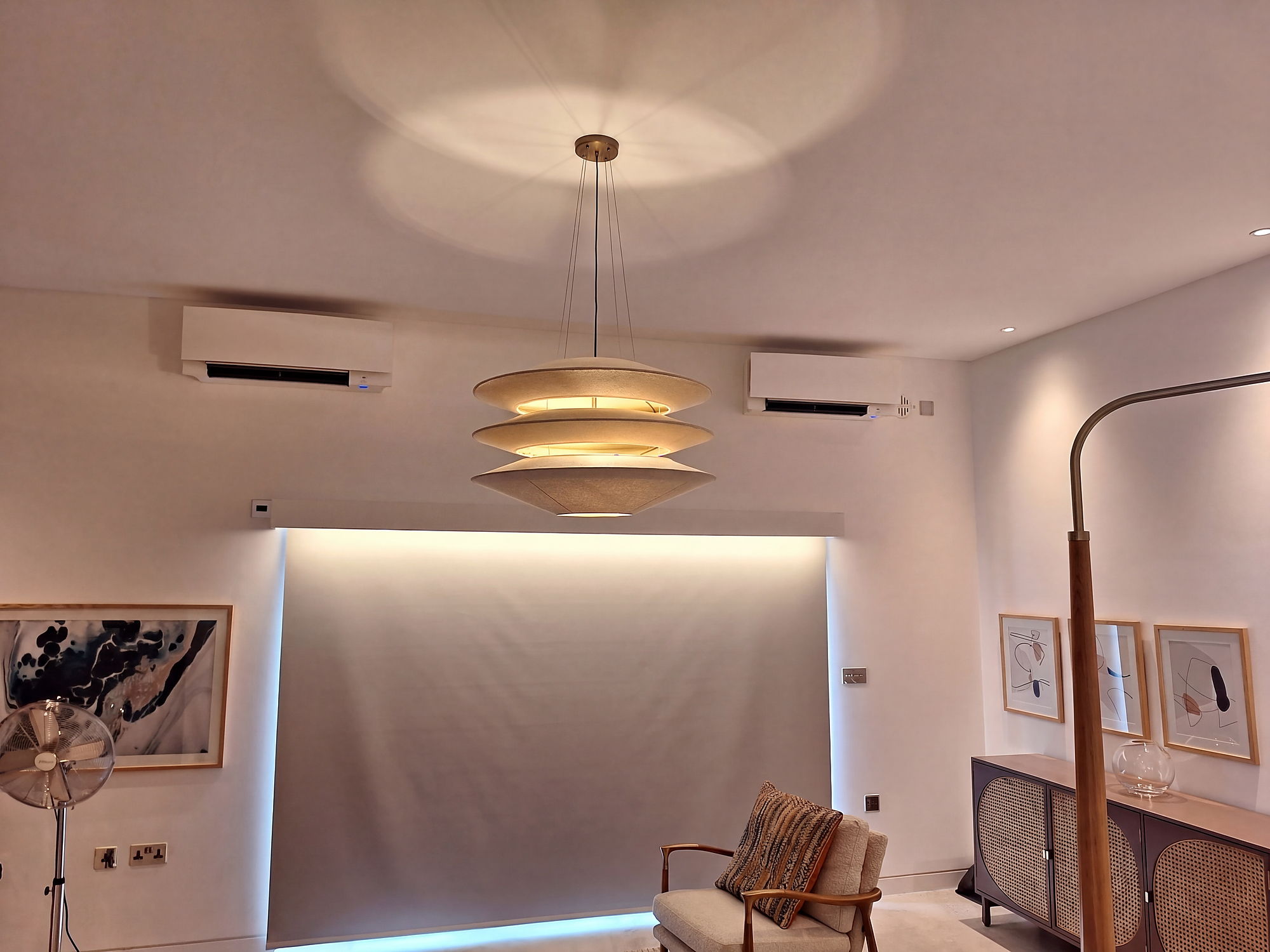 Open plan living room with two wall mounted air conditioning units either side of a designer pendant light