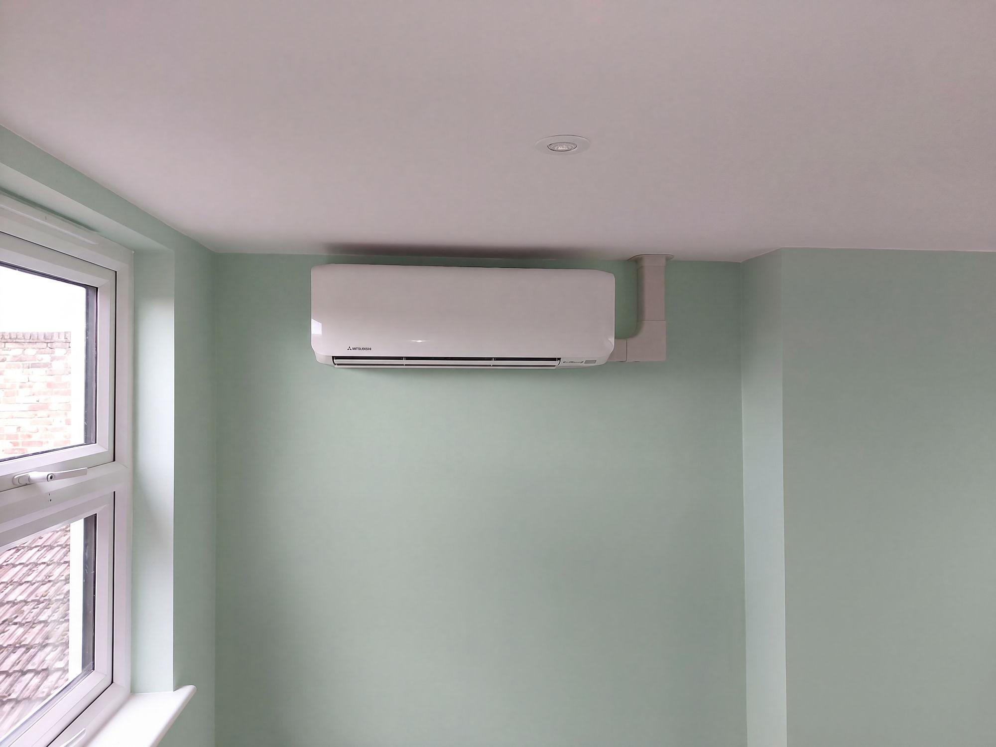 Wall mounted air conditioning unit on a green wall above a cove lit blind